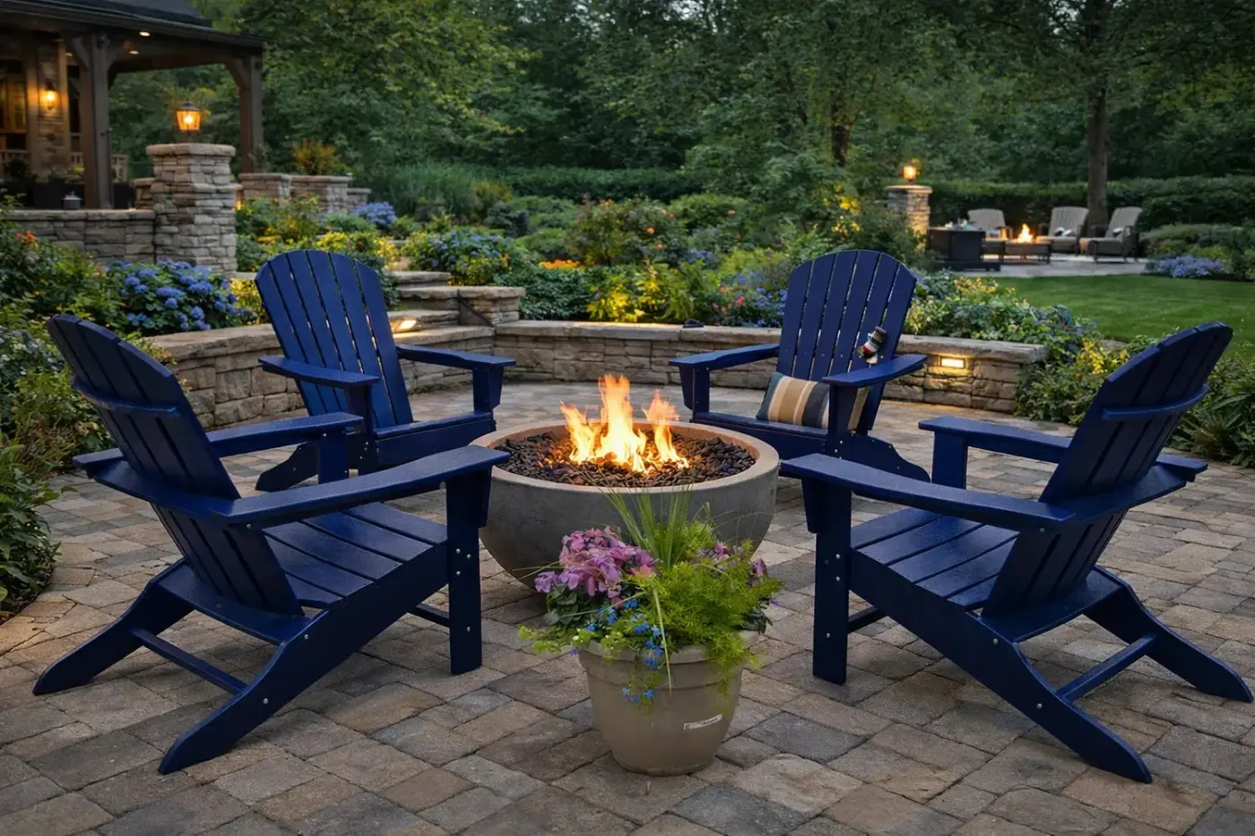 A fire bowl surrounded by navy Adirondack chairs on a garden patio