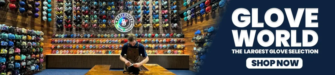 A craftsman working on gloves in front of a wall of baseball caps